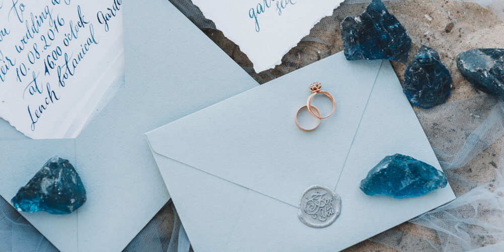 Wedding,And,Engagement,Rings,On,An,Envelope,Next,To,Invitation