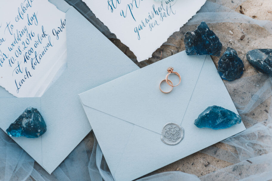 Wedding,And,Engagement,Rings,On,An,Envelope,Next,To,Invitation